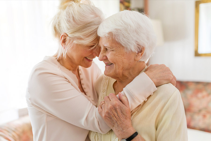 Smiling older woman embracing elderly mother at home