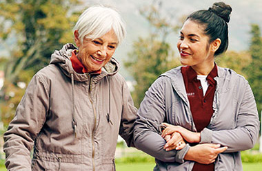 Senior caregiver walking with older woman outdoors providing supportive senior companion care and social connection